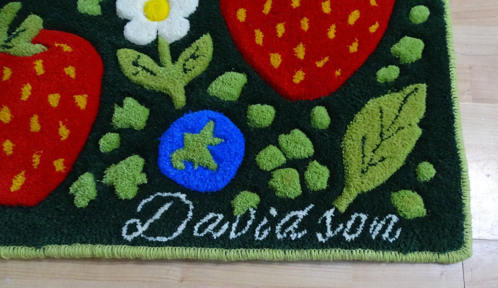 Handgefertigter Kinderteppich mit Erdbeeren, Blaubeeren und Blumen aus 100 % natürlicher baltischer Schafwolle, personalisiert mit dem Namen des Kindes, Draufsicht auf Holzboden