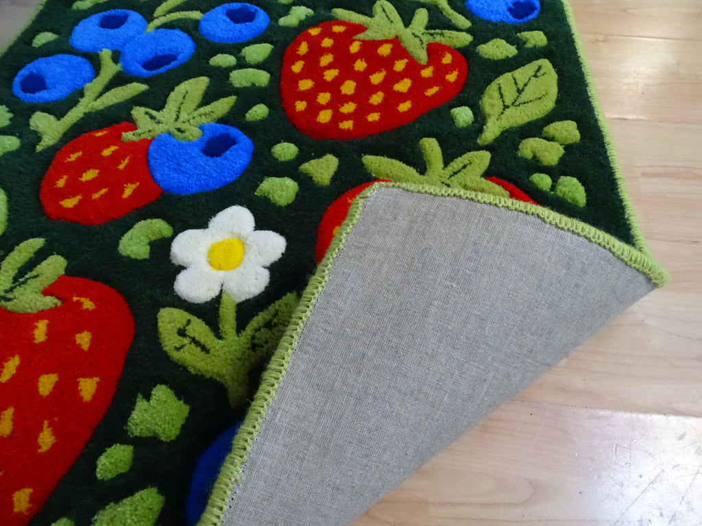 Close-up of a handmade children’s rug showing raised strawberry and blueberry details, carved 3D texture, made from 100% natural Baltic sheep wool