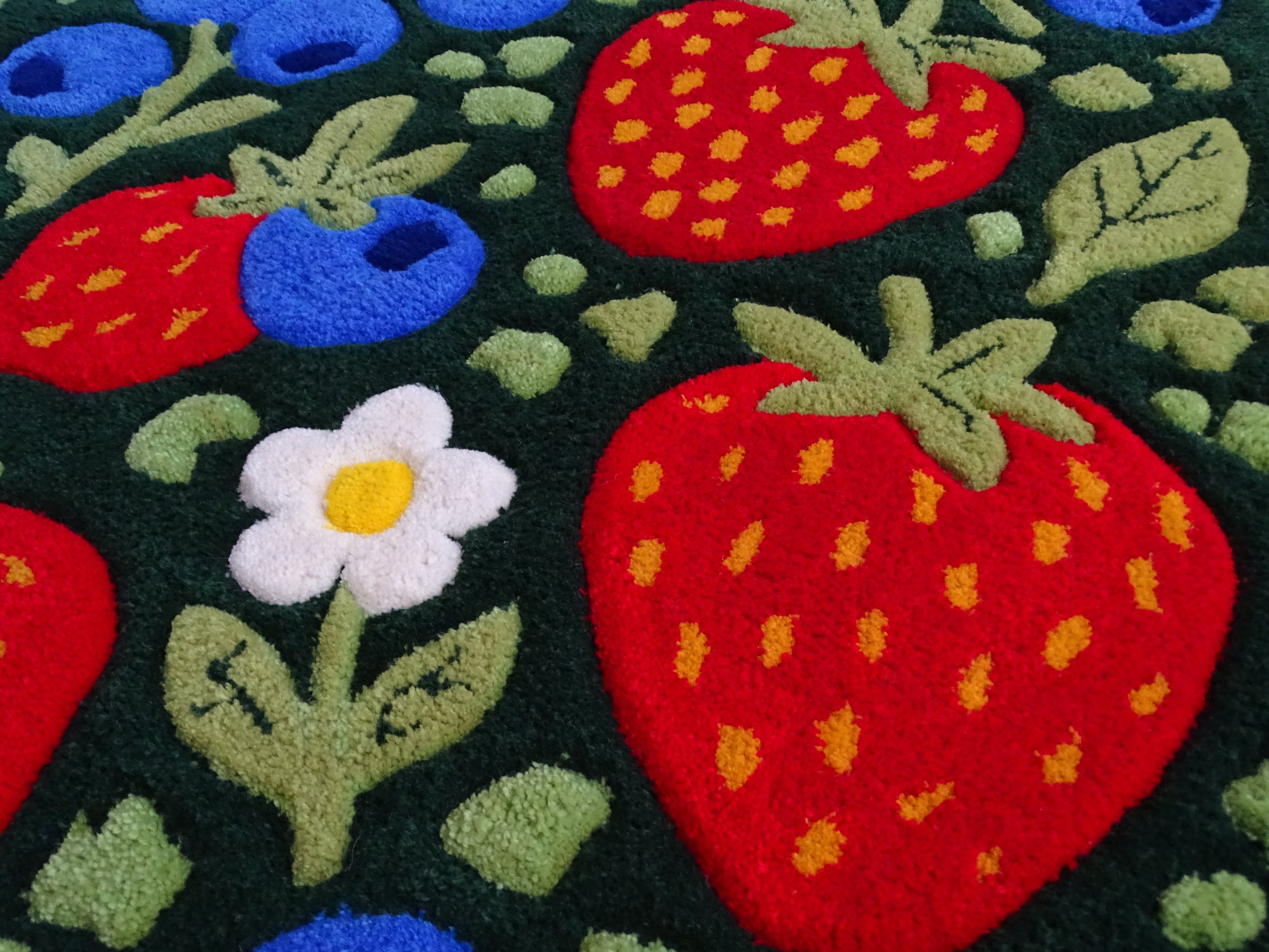 Close-up of a handmade children’s rug showing raised strawberry and blueberry details, carved 3D texture, made from 100% natural Baltic sheep wool