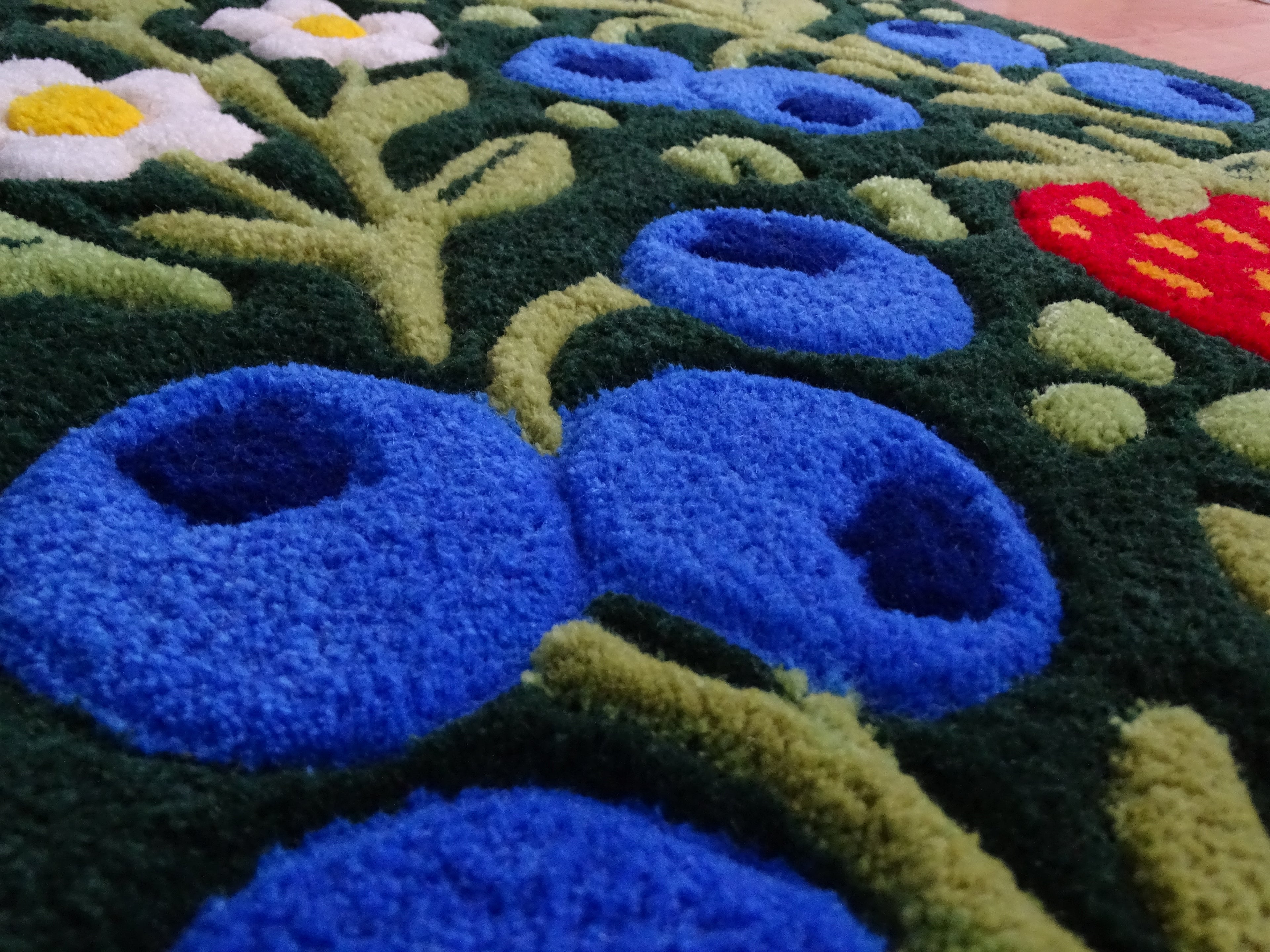 Detailaufnahme eines handgefertigten Kinderteppichs mit erhabenen Erdbeer- und Blaubeer-Motiven, 3D-geschnitzter Struktur aus 100 % natürlicher baltischer Schafwolle