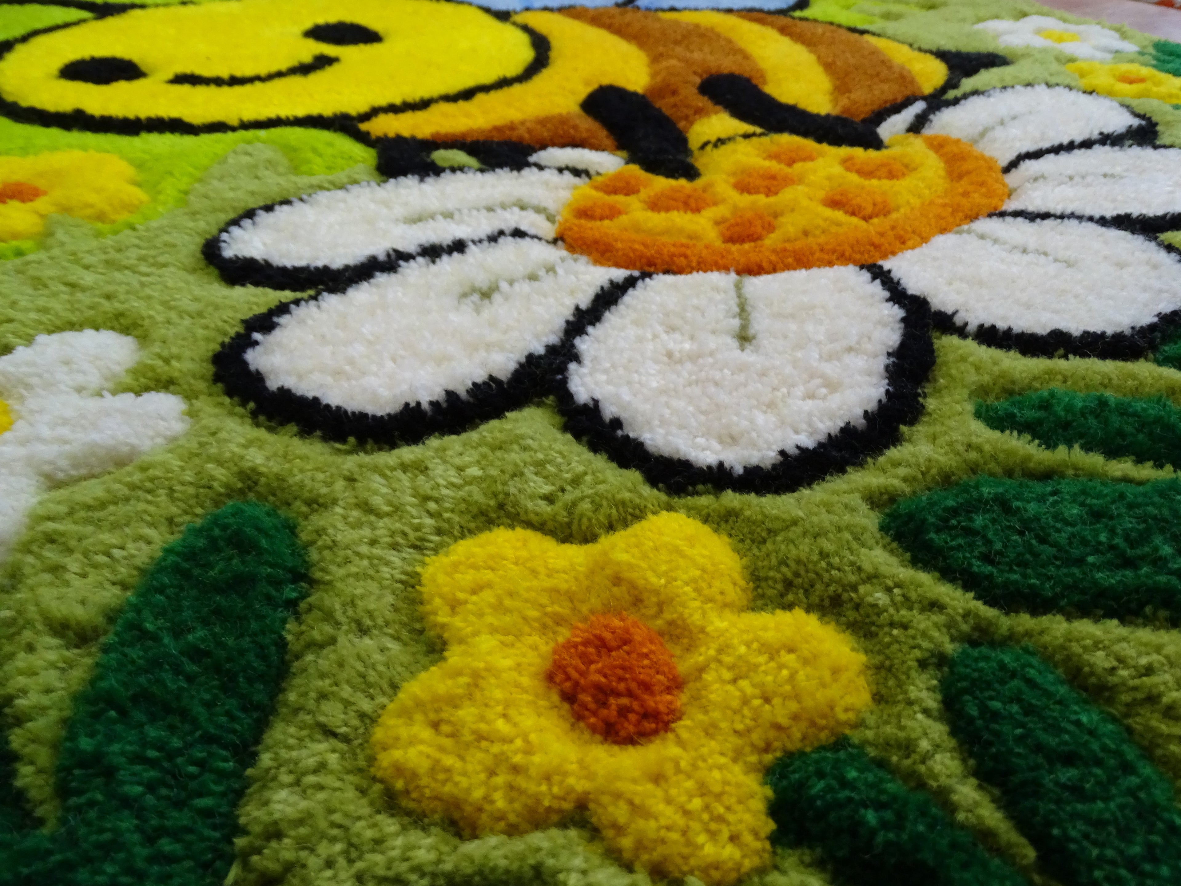 Nahaufnahme der 3D-geschnitzten Schrift auf personalisiertem Wollteppich mit Bienenmotiv, handgefertigt in Lettland.