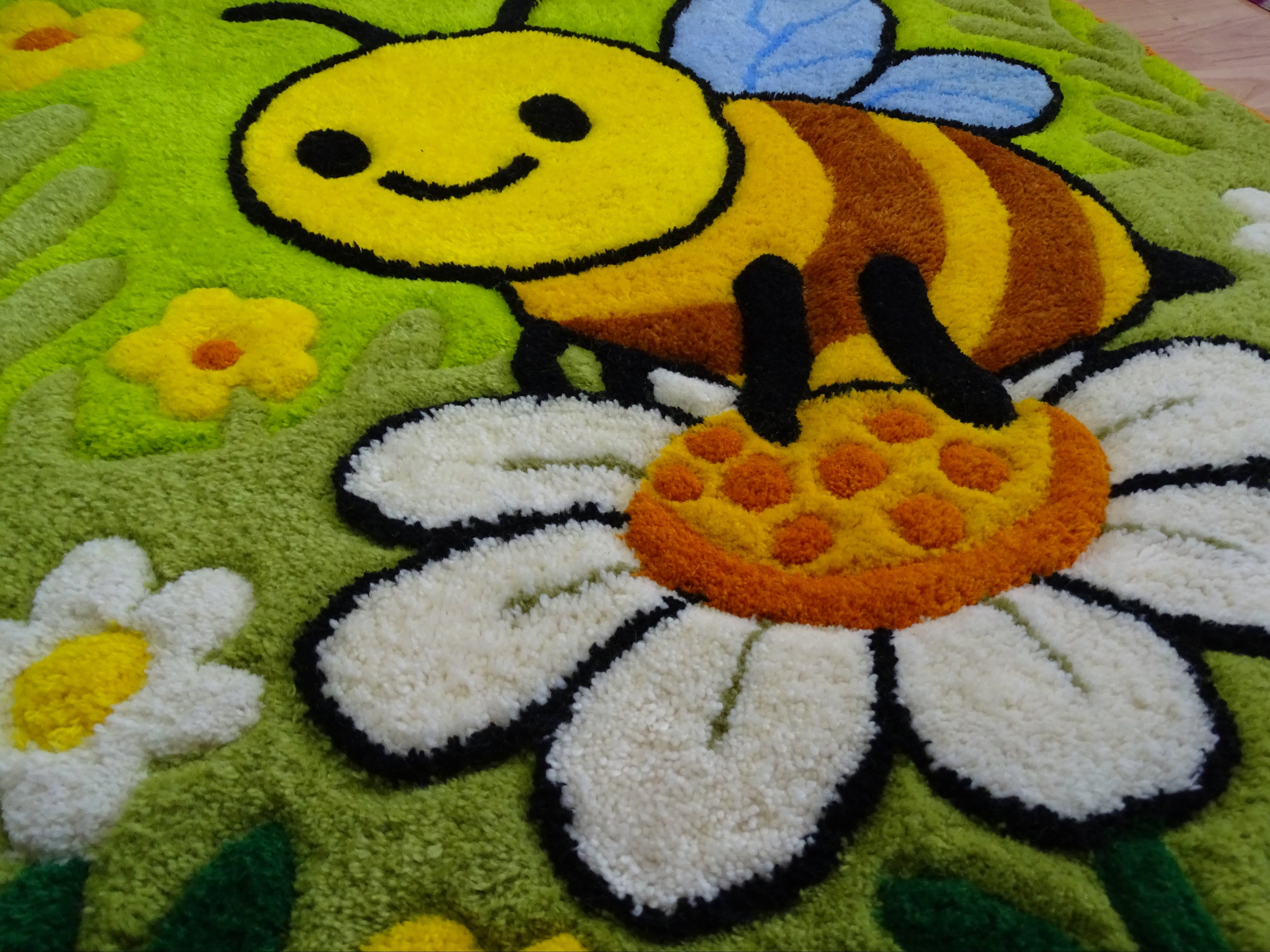 Nahaufnahme der 3D-geschnitzten Schrift auf personalisiertem Wollteppich mit Bienenmotiv, handgefertigt in Lettland.