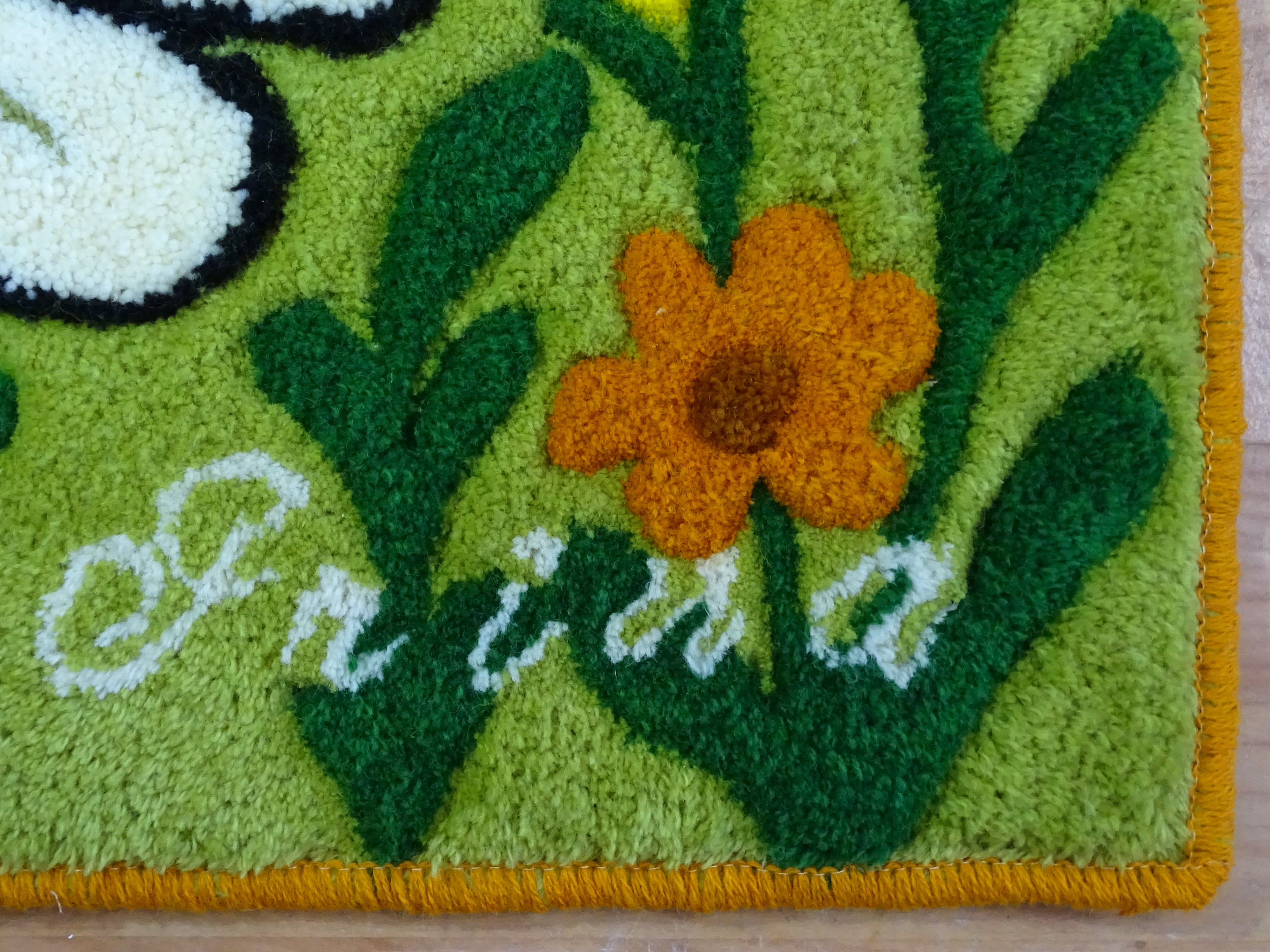 Nahaufnahme der 3D-geschnitzten Schrift auf personalisiertem Wollteppich mit Bienenmotiv, handgefertigt in Lettland.