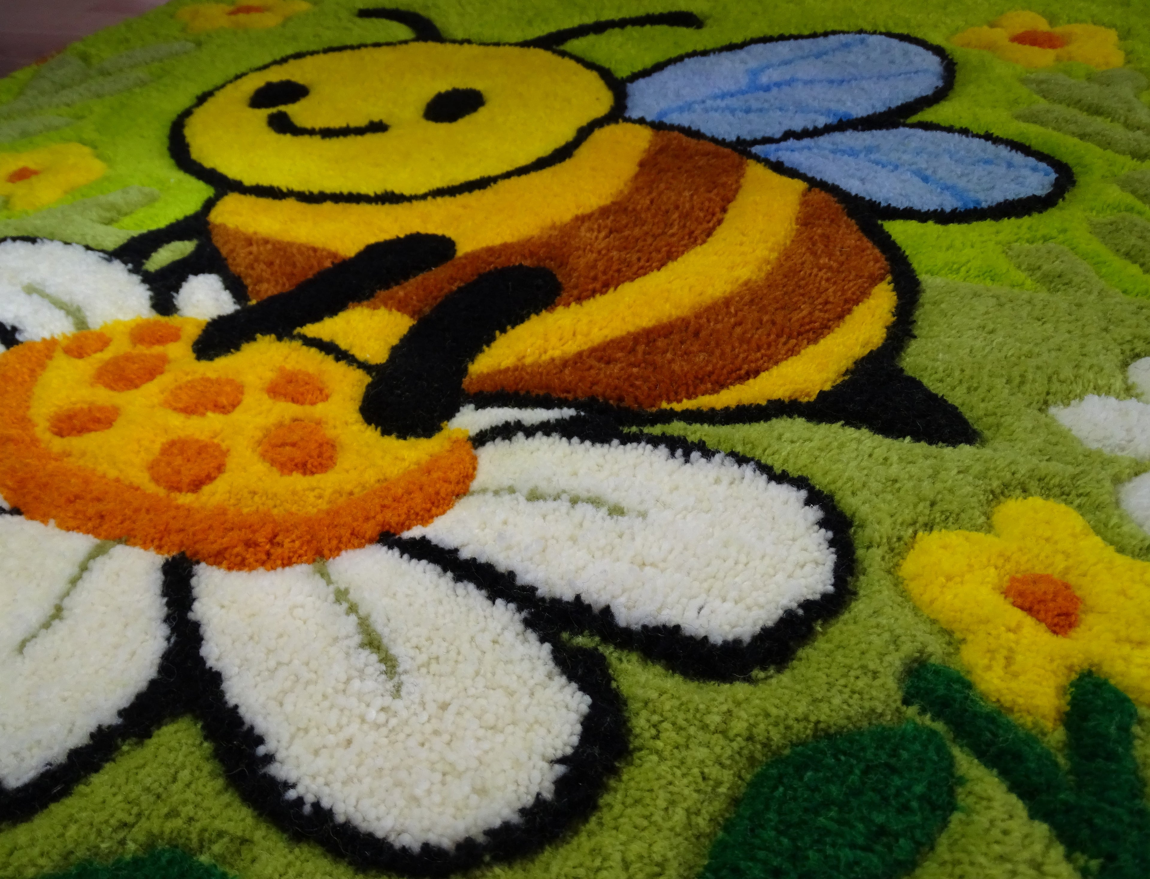 Nahaufnahme der 3D-geschnitzten Schrift auf personalisiertem Wollteppich mit Bienenmotiv, handgefertigt in Lettland.