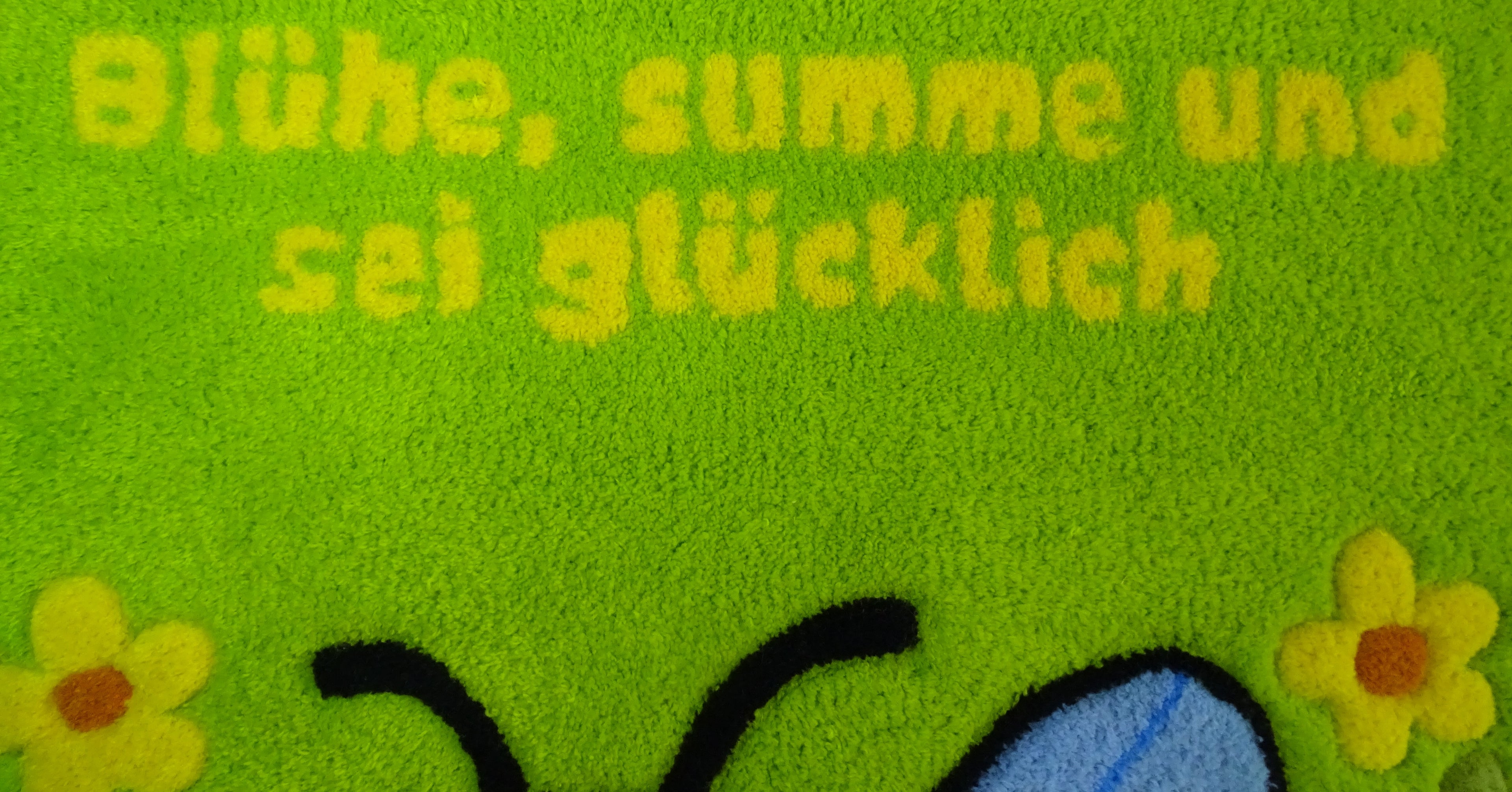 Nahaufnahme der 3D-geschnitzten Schrift auf personalisiertem Wollteppich mit Bienenmotiv, handgefertigt in Lettland.