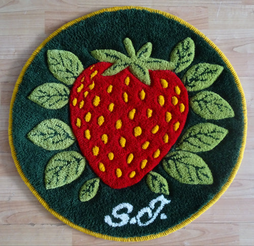 Runder handgetufteter Wollteppich mit Erdbeer-Motiv, personalisiert mit Initialen, mit natürlicher Leinenrückseite auf Holzfußboden fotografiert.