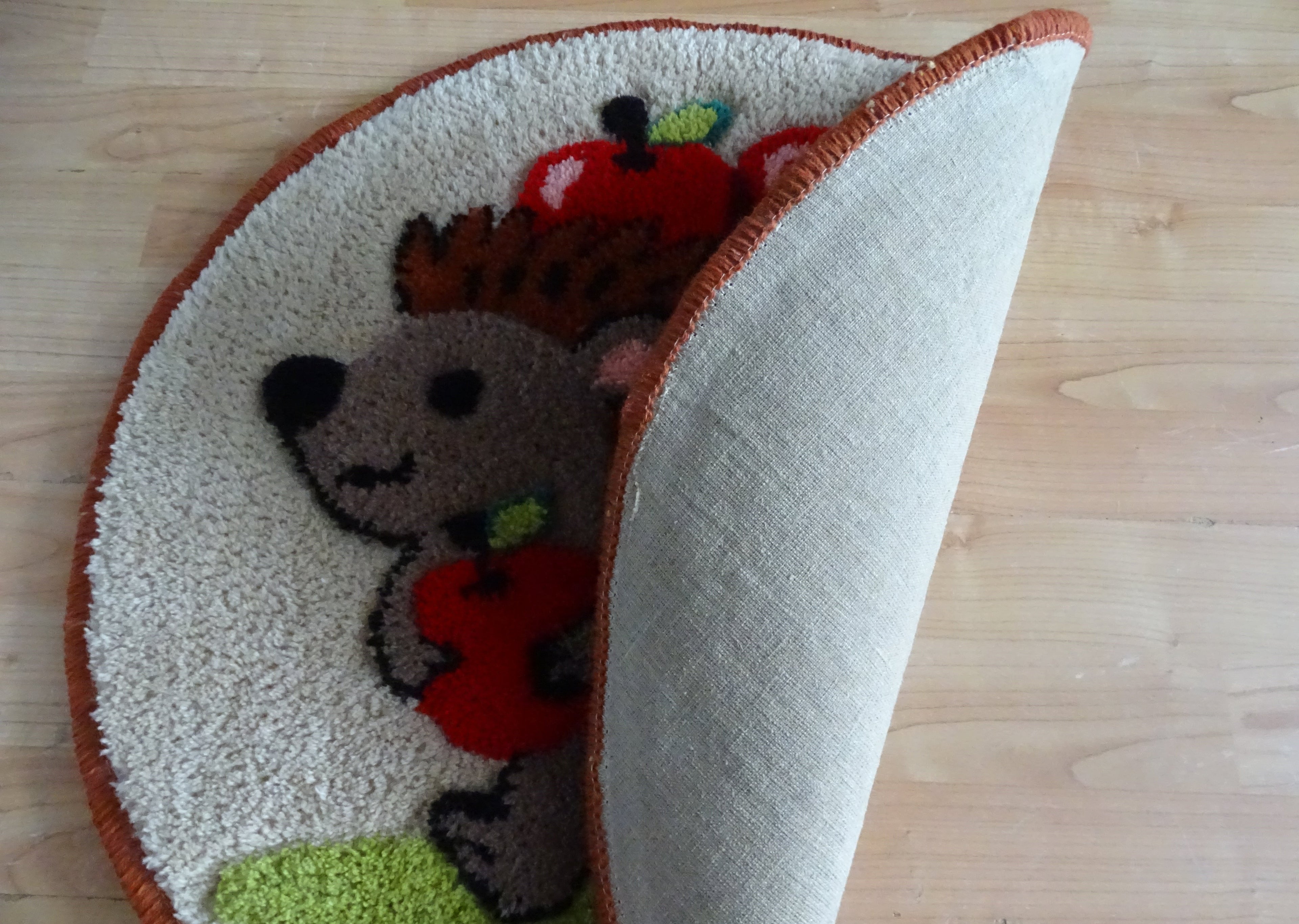 Runder handgetufteter Wollteppich mit Igel-Motiv und Äpfeln, personalisiert mit Initialen, mit natürlicher Leinenrückseite und auf Holzfußboden fotografiert.