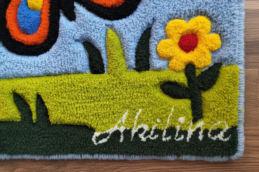 Handgefertigter Kinder-Wollteppich mit buntem Schmetterling und Blumen auf blauem Hintergrund, personalisiert mit dem Namen des Kindes.