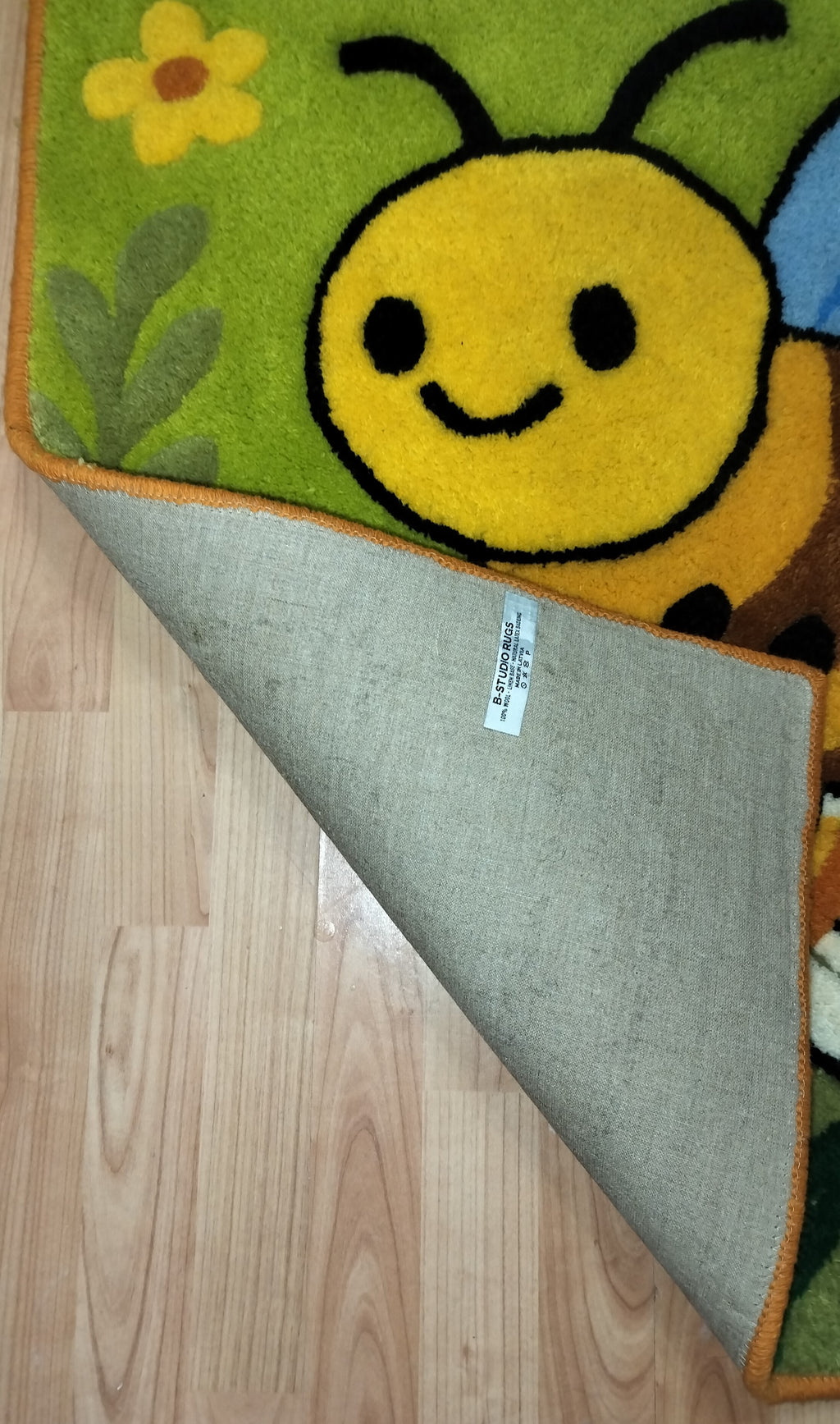 Nahaufnahme der 3D-geschnitzten Schrift auf personalisiertem Wollteppich mit Bienenmotiv, handgefertigt in Lettland.