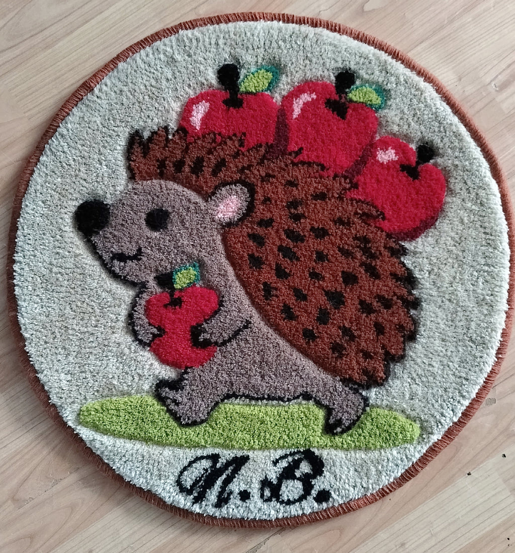 Runder handgetufteter Wollteppich mit Igel-Motiv und Äpfeln, personalisiert mit Initialen, auf Holzfußboden fotografiert.